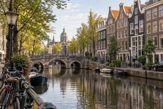 Amsterdam canal houses, a stone arch bridge and bicycles beside the water.